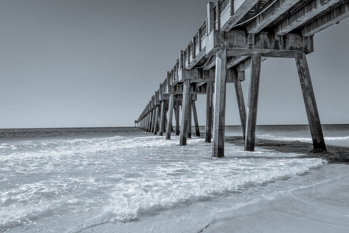 Long wooden pier extending into the ocean with waves crashing against the shore.