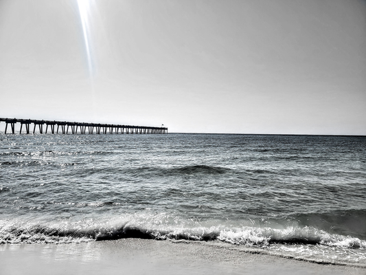 Black and white photo of a pier extending into the ocean with waves crashing on the shore.